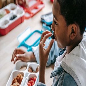 African American elementary school male eating a blueberry.