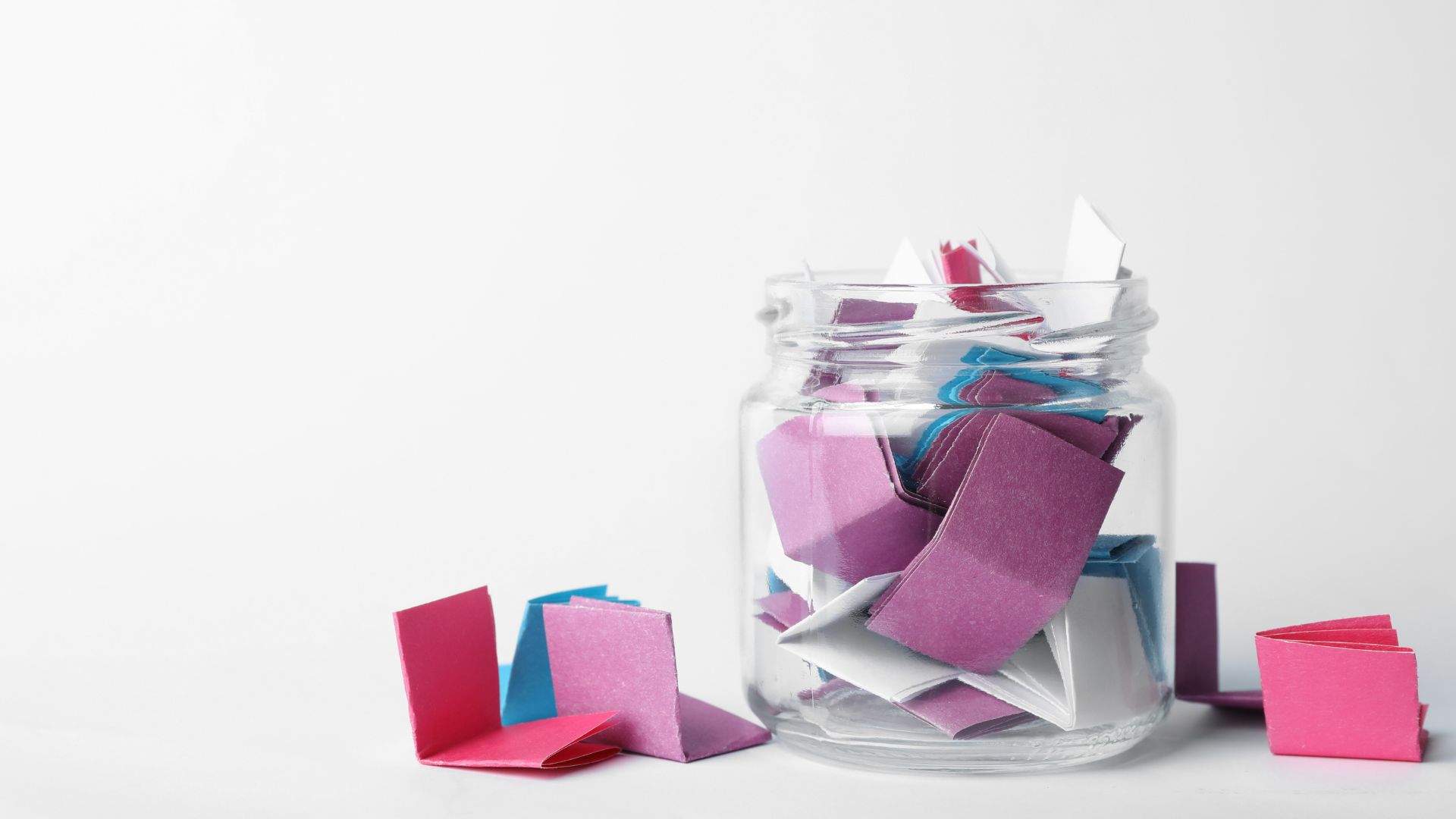 Clear jar with small folded pieces of different color paper inside.
