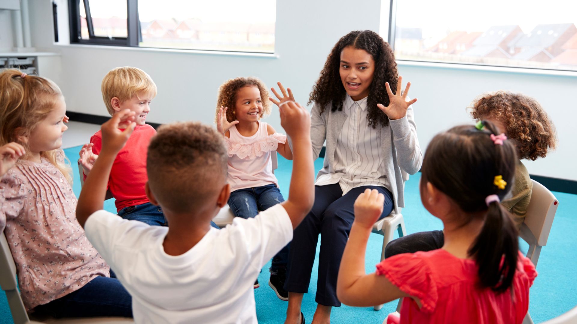 Five children and one teacher sitting on chairs in a circle.