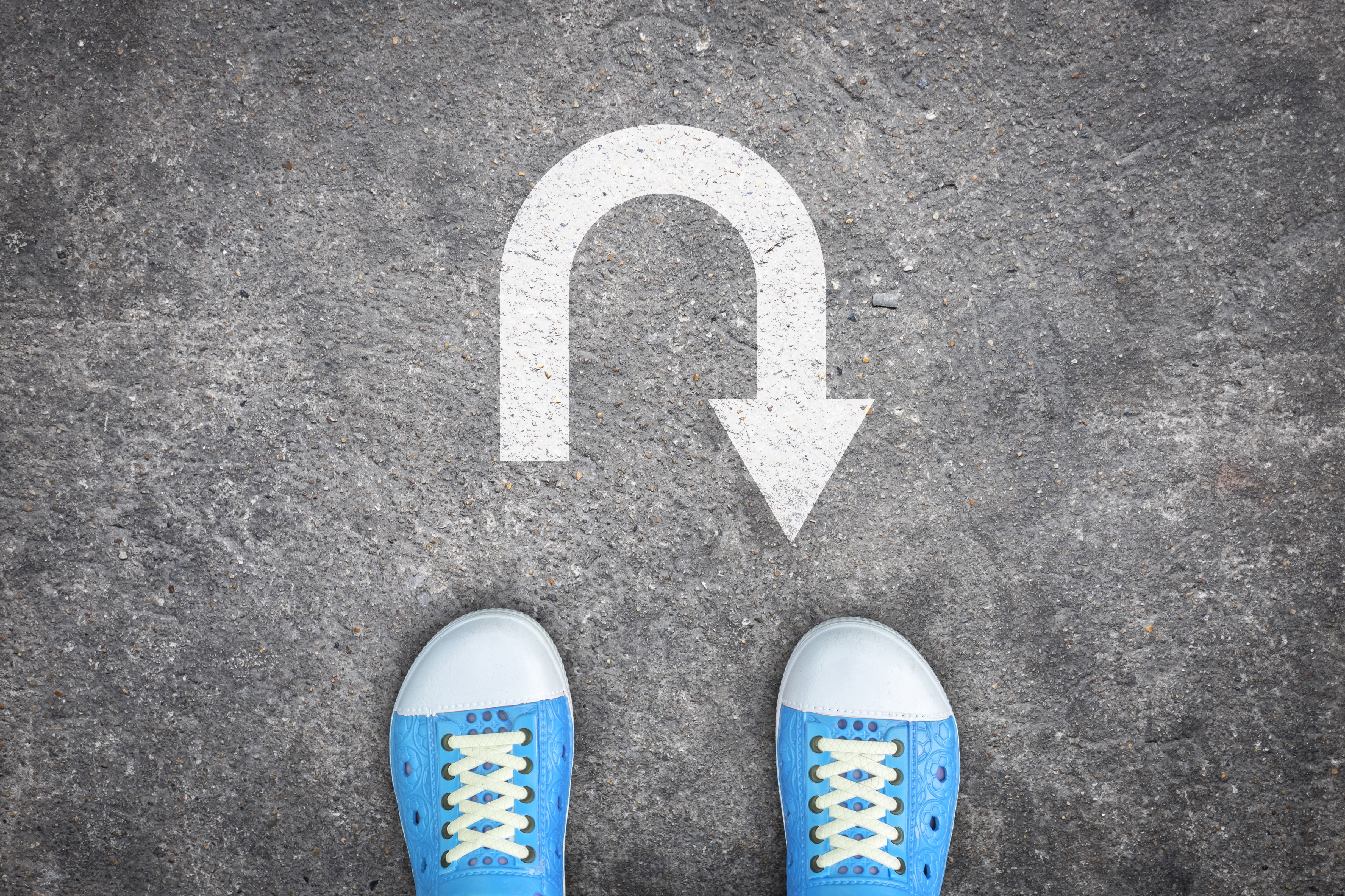 Person wearing blue shoes standing on pavement with a u-turn arrow in front of them.