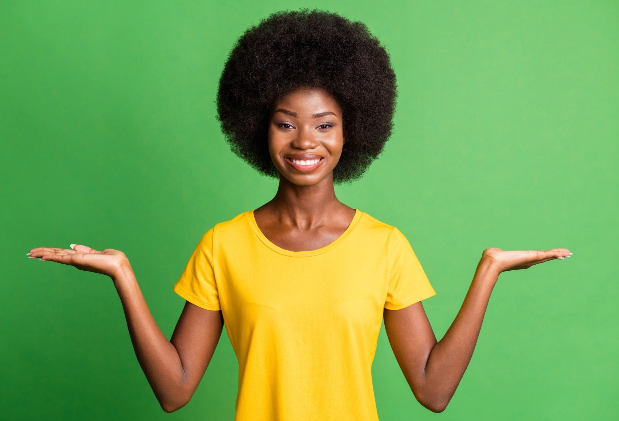 African American woman with natural hair, wearing a yellow shirt, holding out both hands to the side.