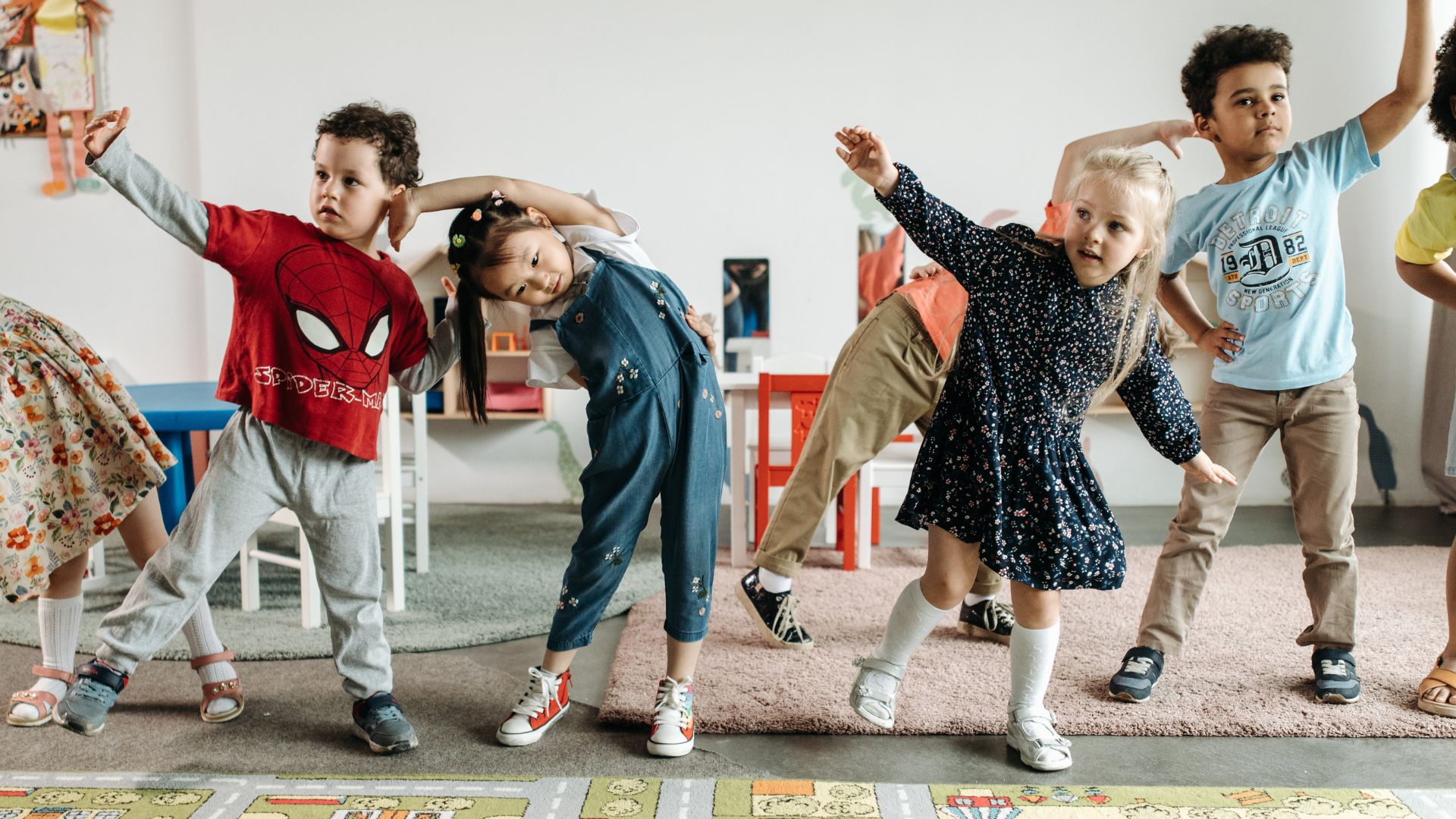 Group of preschool children all making stretching poses with one arm over their heads.